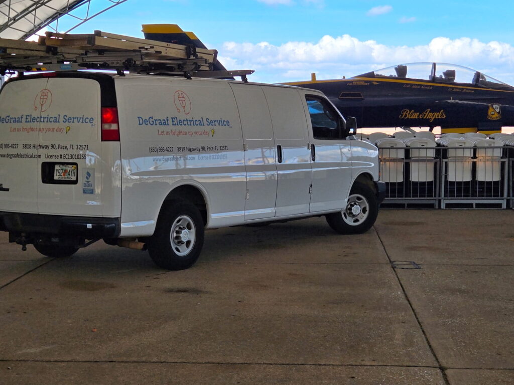 DeGraaf Electrical Service vehicle parked beside a F/A-18 hornet Blue Angel aircraft at the Naval Aviation Museum.