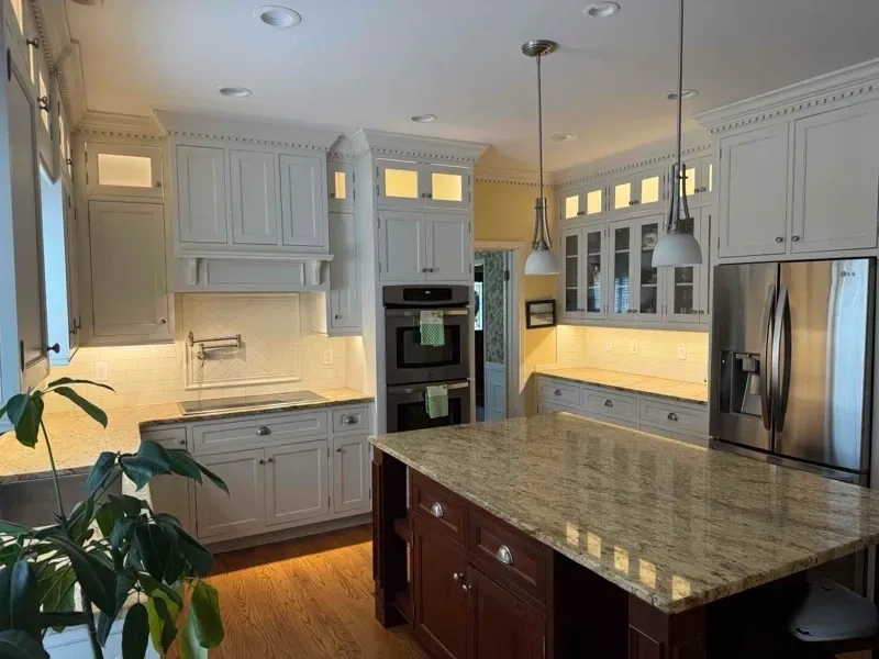 A photo of a kitchen with white cabinets with under cabinet lighting and lighting inside the upper cabinets.