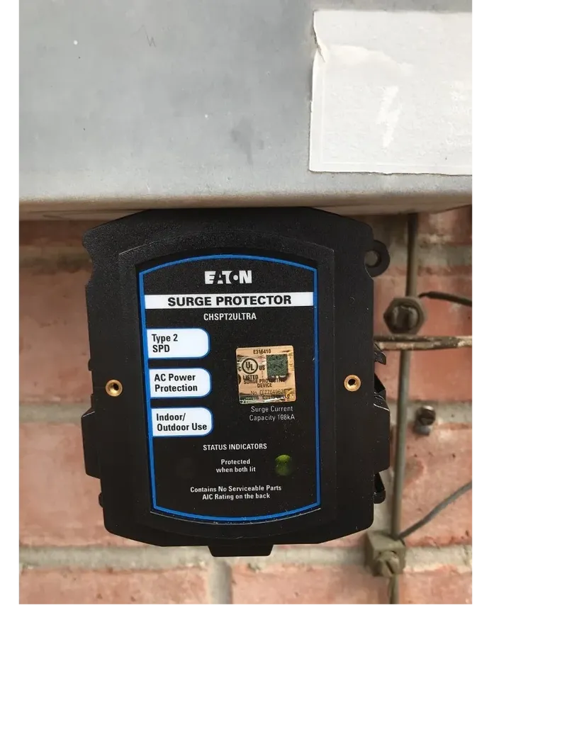 A whole house surge protector mounted to the bottom of an electrical service panel.