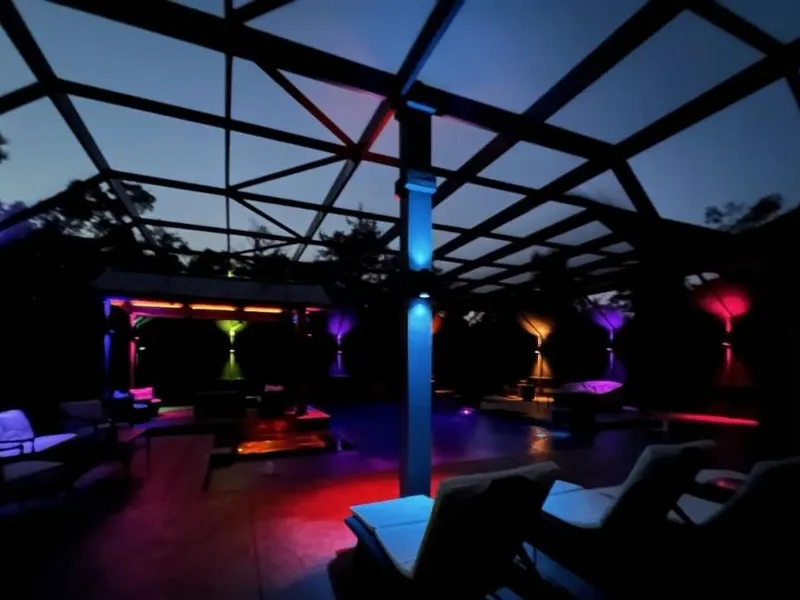 A photo of color changing ambience lighting mounted to the support beams of a screened in pool enclosure around a pool.