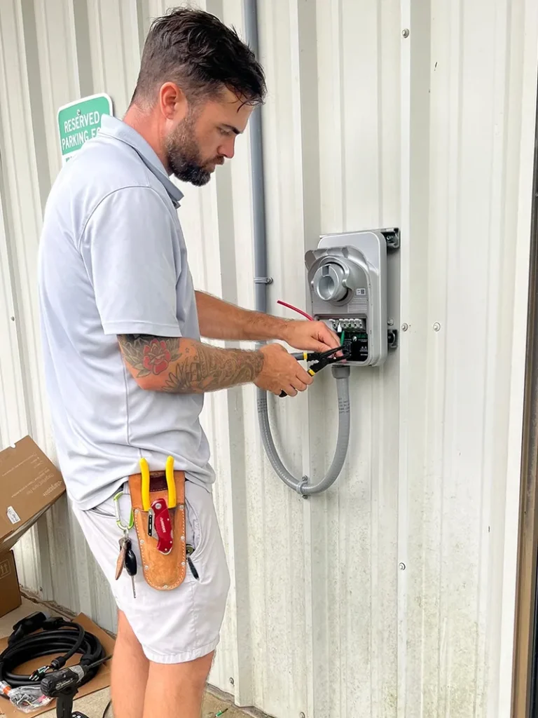 An electrician mounting an EV charging unit to a metal wall at a business and terminating electrical wires inside the EV charging unit.