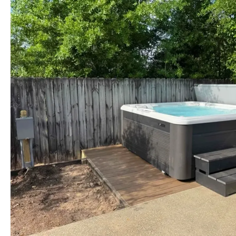 A photo of an uncovered hot tub with steps, sitting on a wood deck with a hot tub disconnect panel to the left.