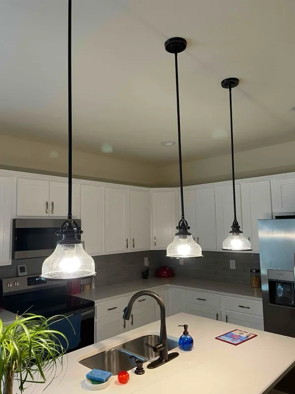 Three matching pendant light fixtures mounted over a kitchen island at a home in Pace, FL.