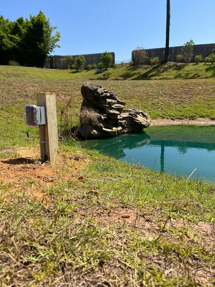 An electrical outlet installed on a post with weather resistant cover for a pond water feature.