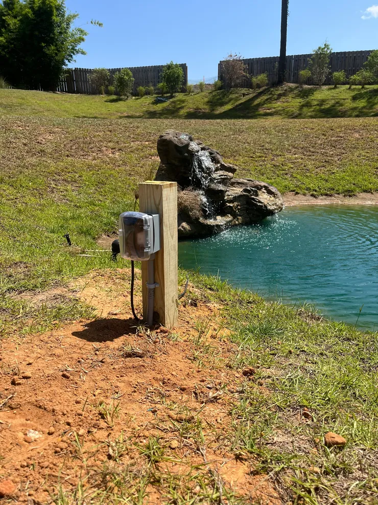A weather resistant outlet installed on a post beside a pond for a water feature.