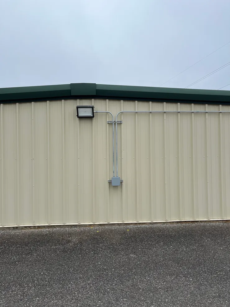 A wall pack light fixture and electrical metal conduit installed on the outside of a storage building.