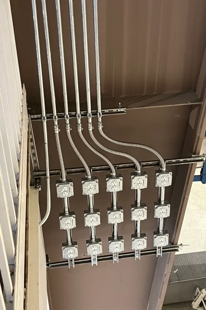 Fifteen receptacles installed in individual metal boxes mounted to a unistrut rack on a iron support beam.