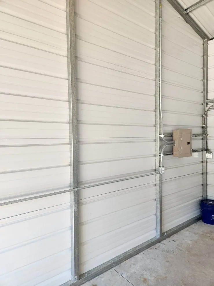 An electrical panel, wiring, receptacles, and conduit installed in a metal shed building.