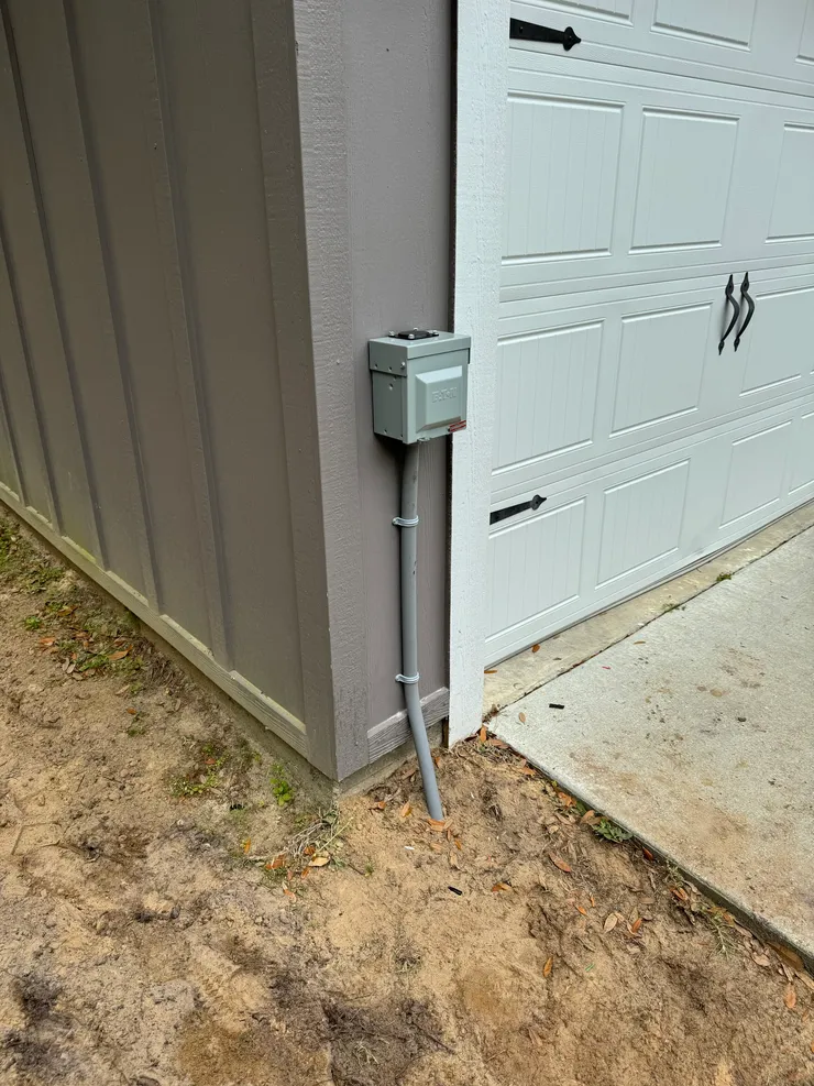 An RV receptacle mounted on the exterior wall beside the garage door at a home in Milton, FL.