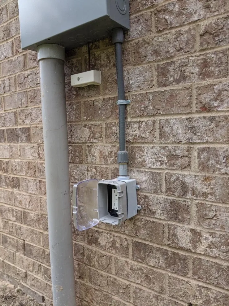 A receptacle installed in a weather proof box and cover beneath an exterior electrical panel.