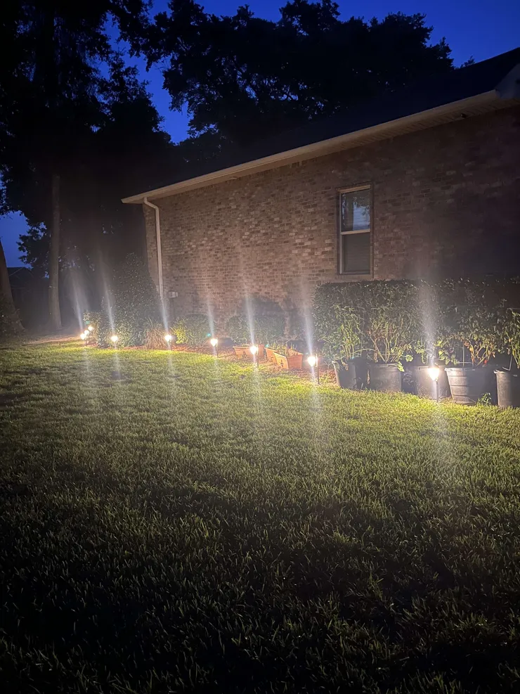 A night time photo of landscape pathway lighting around a flower bed.
