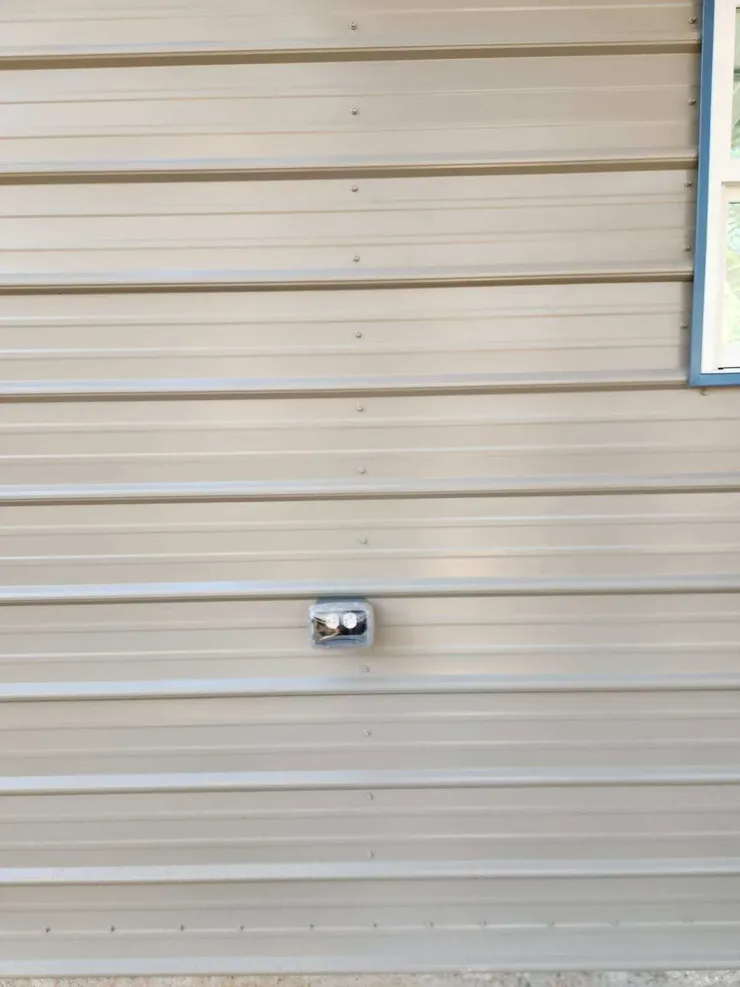 Electrical receptacle installed in weather proof box and cover on the exterior of a metal shed.